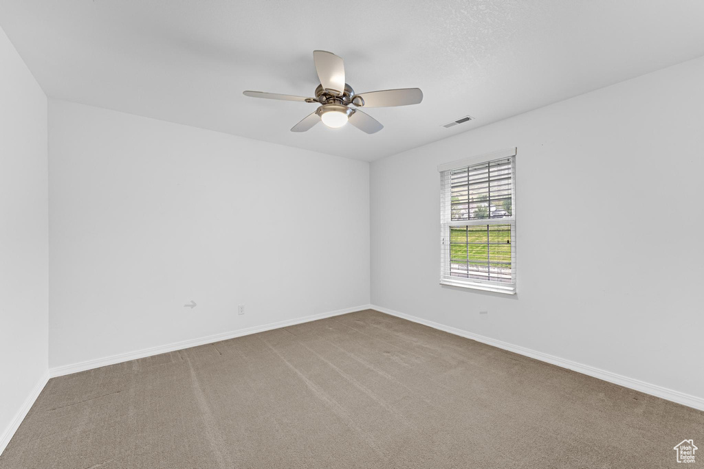 Spare room featuring carpet flooring, baseboards, visible vents, and ceiling fan