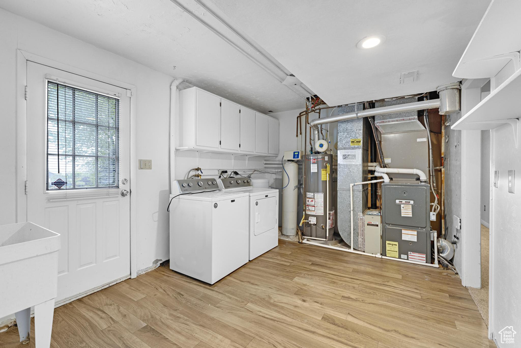 Laundry room featuring water heater, light wood finished floors, cabinet space, and washer and clothes dryer