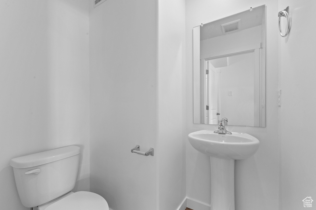 Half bath with toilet, baseboards, visible vents, and a sink