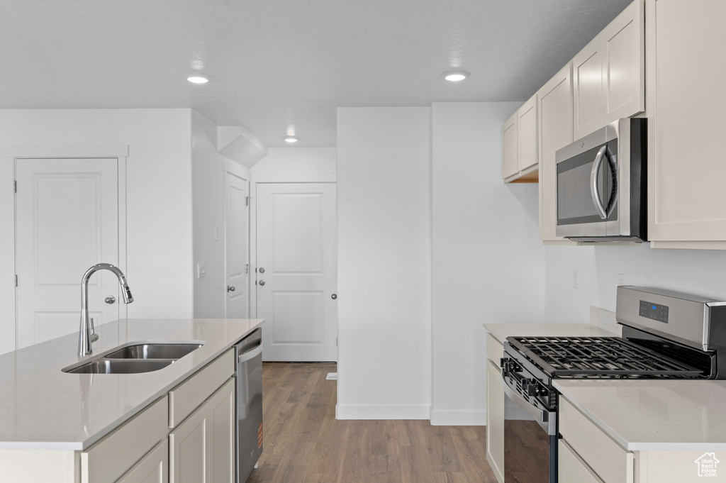 Kitchen with appliances with stainless steel finishes, a sink, a kitchen island with sink, recessed lighting, and light wood-type flooring