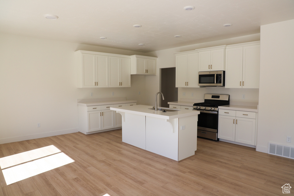 Kitchen featuring a kitchen island with sink, visible vents, appliances with stainless steel finishes, a sink, and light wood finished floors