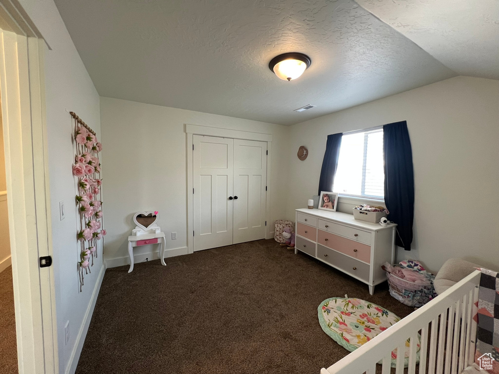 Bedroom featuring a closet, dark carpet, baseboards, a textured ceiling, and vaulted ceiling