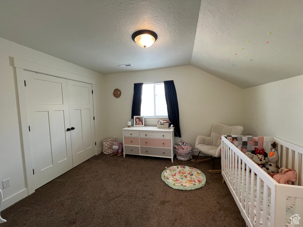 Bedroom featuring a textured ceiling, visible vents, a nursery area, lofted ceiling, and dark carpet