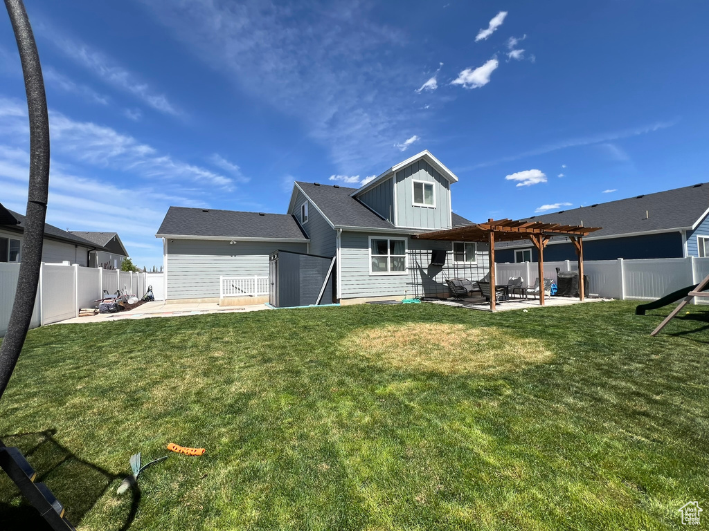 Rear view of house with a pergola, board and batten siding, a fenced backyard, a lawn, and a patio