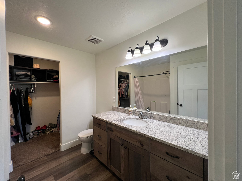 Full bathroom with visible vents, vanity, wood finished floors, toilet, and a walk in closet