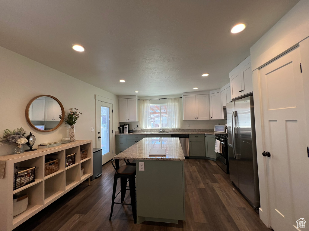 Kitchen with stainless steel appliances, light stone counters, dark wood finished floors, and a center island