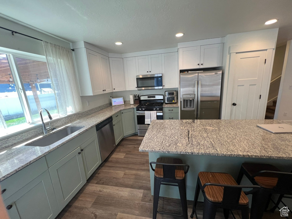 Kitchen with dark wood-style flooring, a breakfast bar, light stone countertops, a sink, and appliances with stainless steel finishes