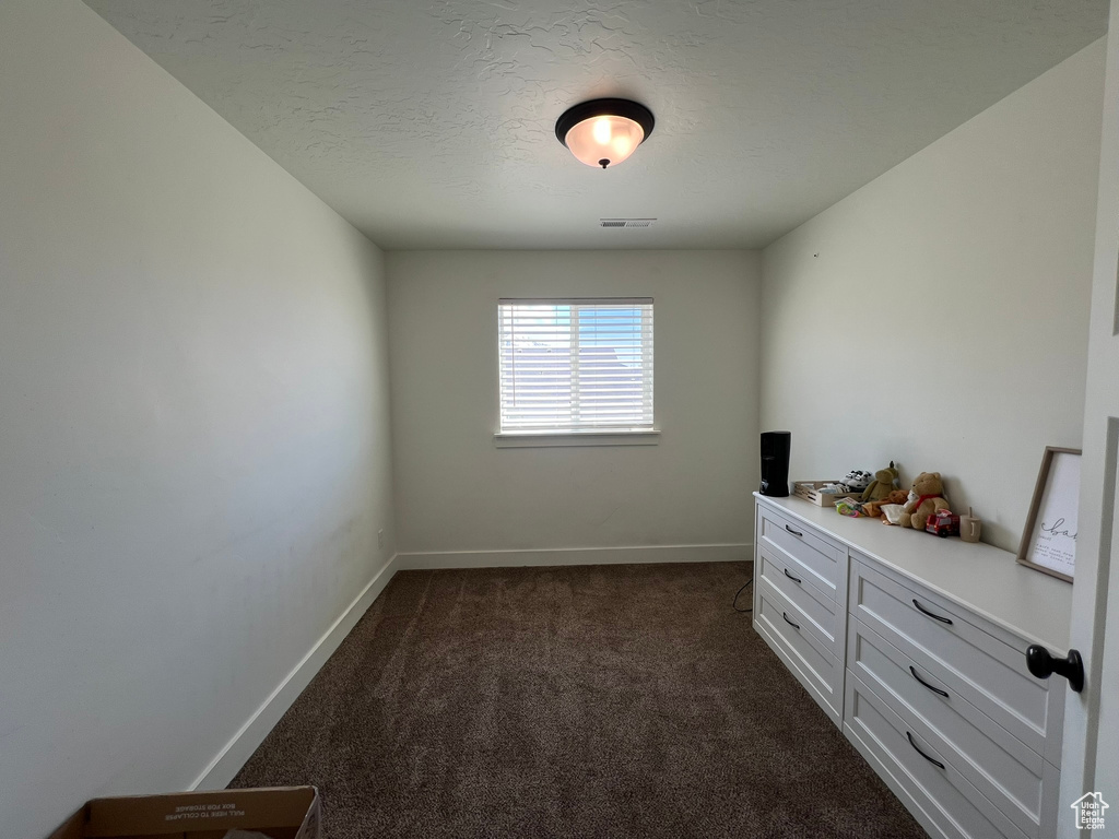 Unfurnished room featuring a textured ceiling, baseboards, visible vents, and dark carpet