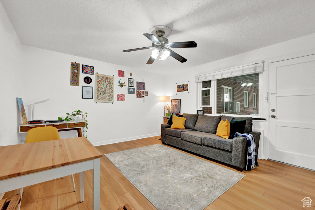 Living area featuring light wood-style floors, baseboards, a ceiling fan, and a textured ceiling