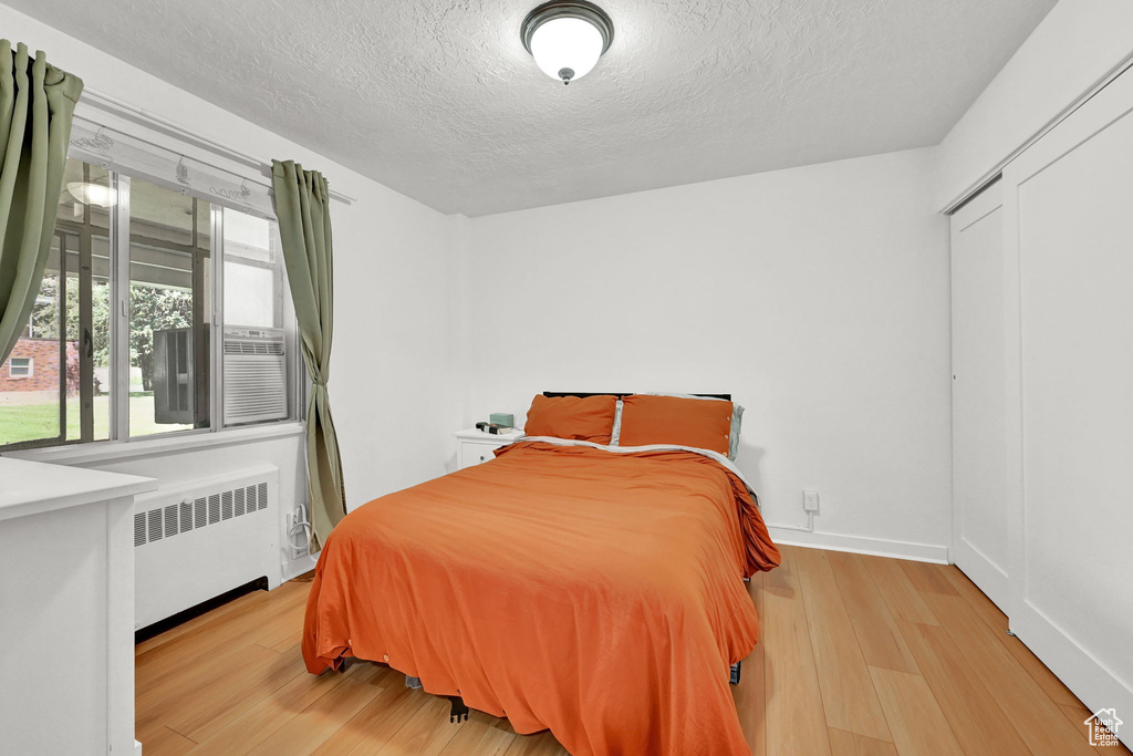 Bedroom with radiator, baseboards, a textured ceiling, and wood finished floors