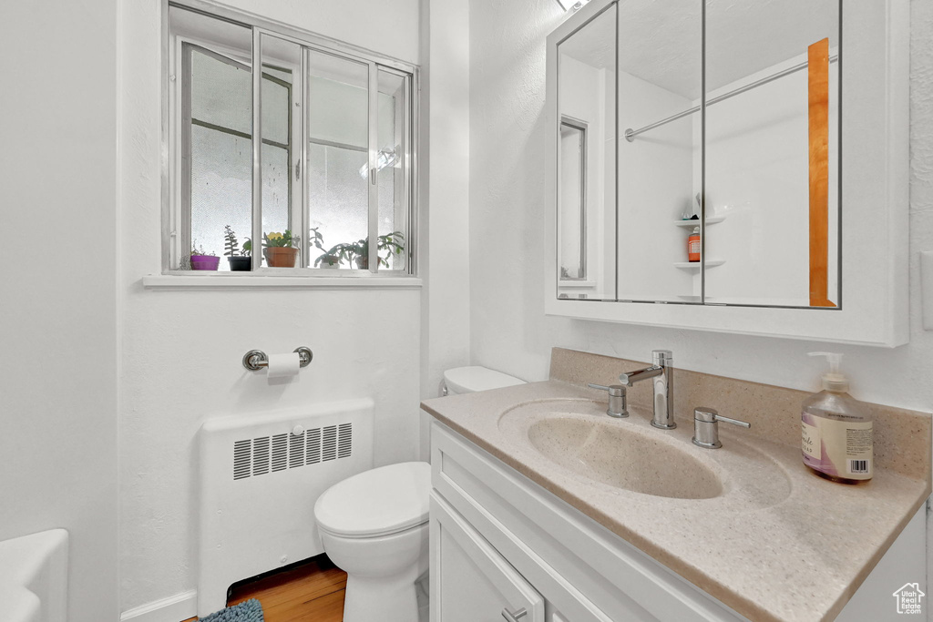 Bathroom with radiator heating unit, vanity, toilet, and wood finished floors