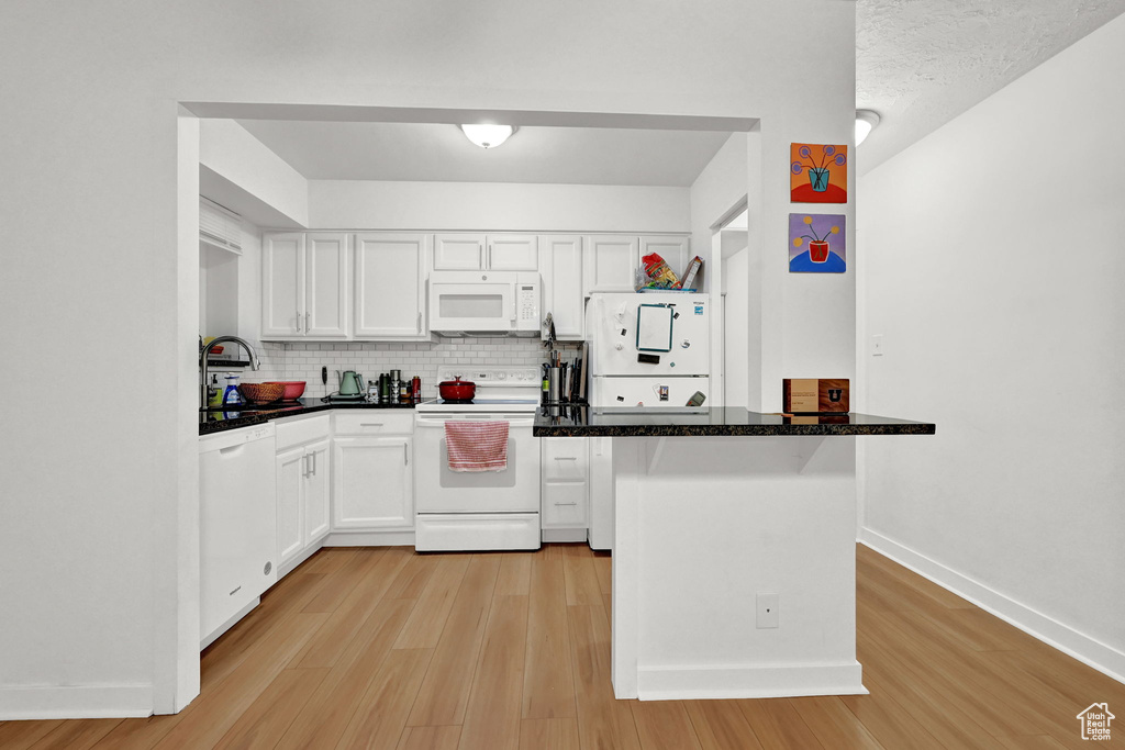 Kitchen with light wood-type flooring, a sink, white cabinets, and white appliances