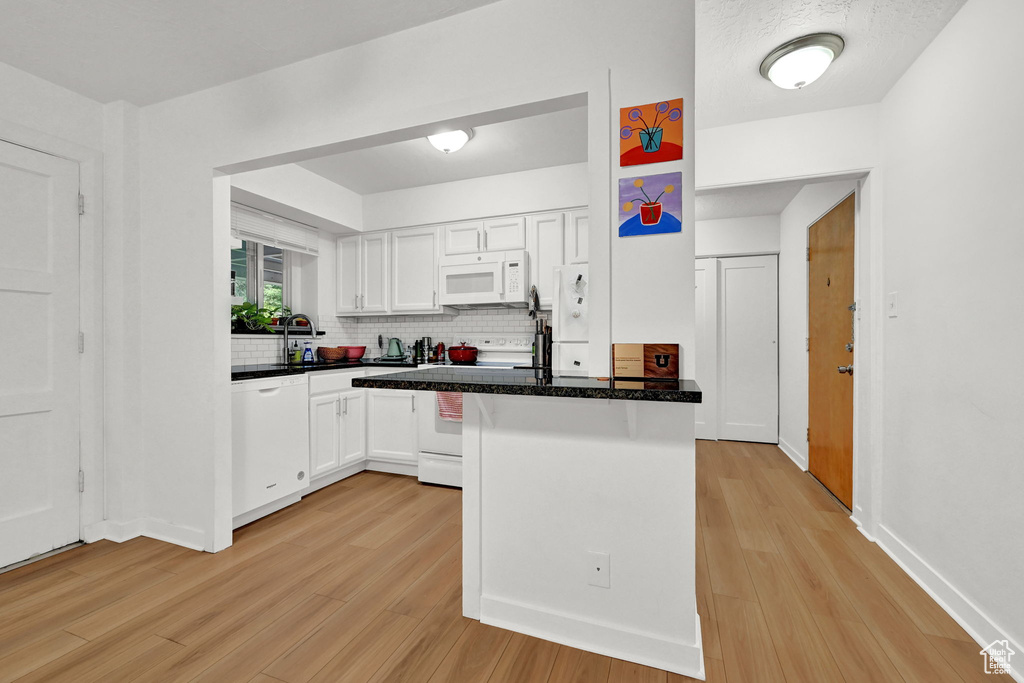 Kitchen featuring light wood finished floors, white appliances, white cabinetry, a peninsula, and backsplash