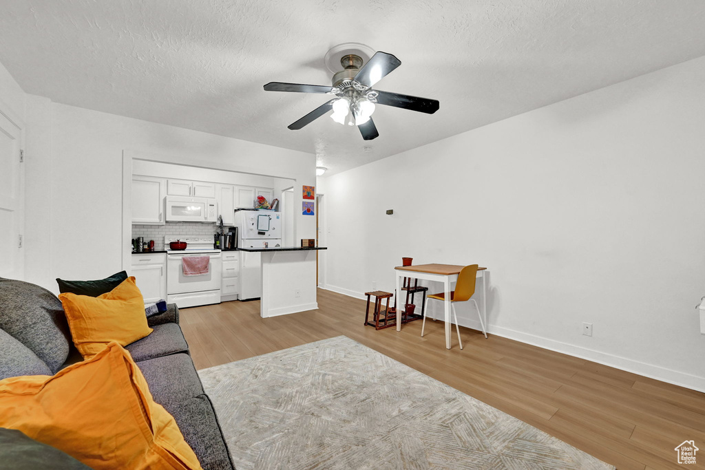 Living room with a textured ceiling, ceiling fan, baseboards, and light wood-style floors