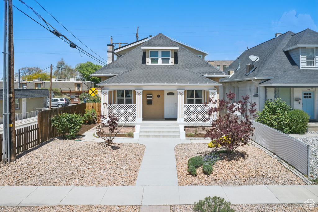 View of front of house featuring fence, covered porch, and a shingled roof