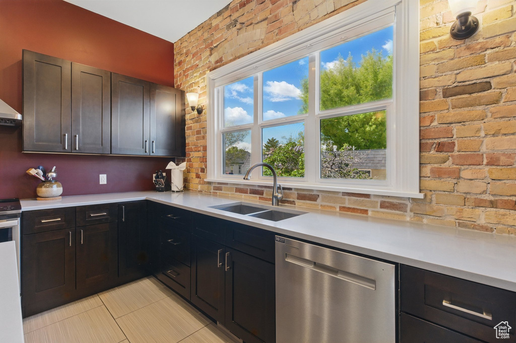 Kitchen with a sink, light countertops, brick wall, light tile patterned floors, and stainless steel dishwasher