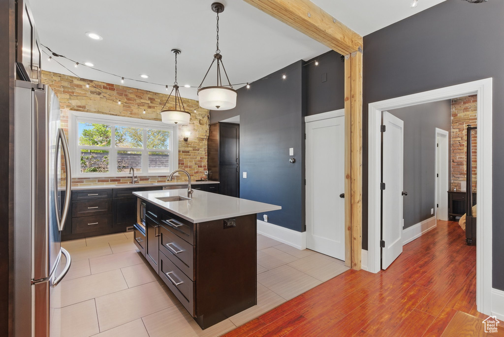 Kitchen with dark brown cabinetry, a sink, light countertops, freestanding refrigerator, and a center island with sink
