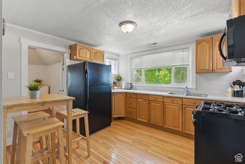 Kitchen with a sink, light countertops, light wood-type flooring, visible vents, and black appliances