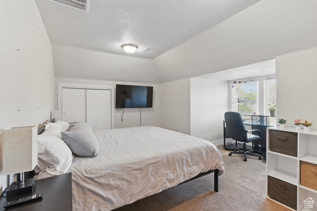 Bedroom with vaulted ceiling, light colored carpet, visible vents, and a closet