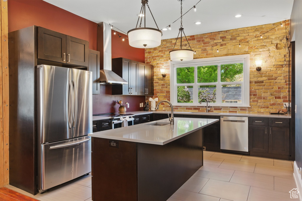Kitchen featuring wall chimney range hood, hanging light fixtures, a sink, light countertops, and stainless steel appliances