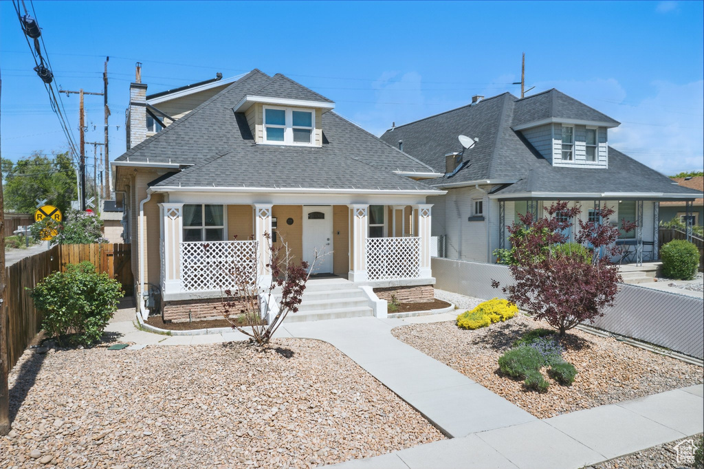 View of front of house featuring covered porch, fence, a shingled roof, and a chimney