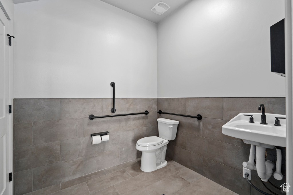 Bathroom with toilet, tile walls, tile patterned flooring, and a wainscoted wall