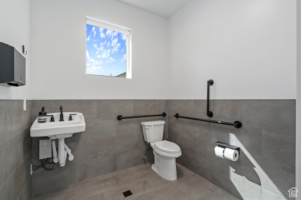Half bath with tile walls, tile patterned flooring, a wainscoted wall, and toilet