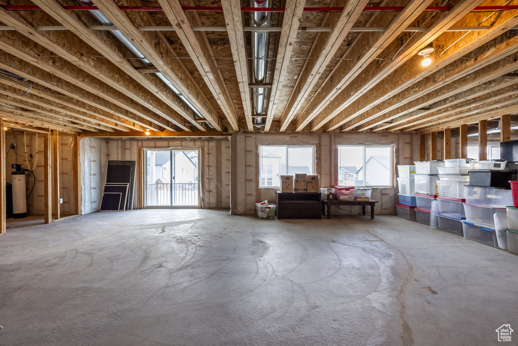 Misc room with unfinished concrete floors, plenty of natural light, and water heater