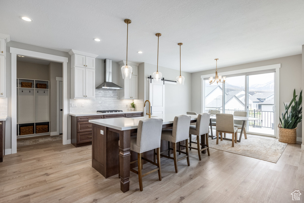 Kitchen with light wood finished floors, light countertops, wall chimney range hood, stainless steel gas stovetop, and decorative backsplash