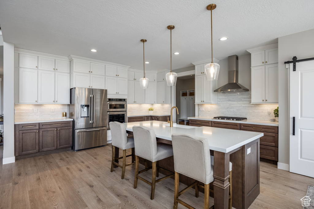 Kitchen featuring stainless steel appliances, tasteful backsplash, light countertops, and wall chimney range hood