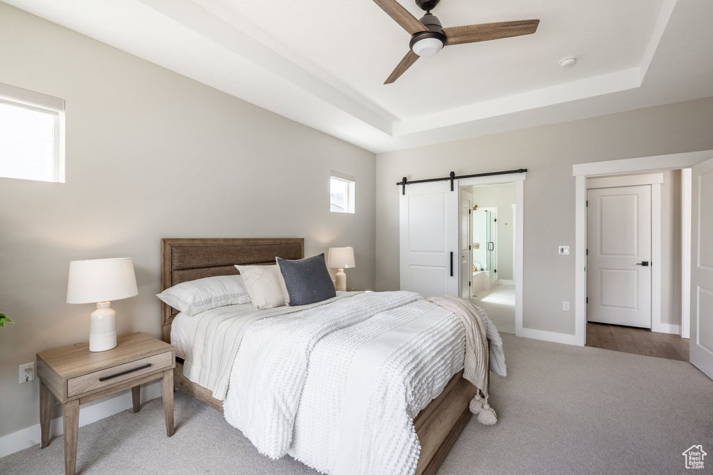Bedroom with baseboards, a barn door, a raised ceiling, ceiling fan, and light carpet