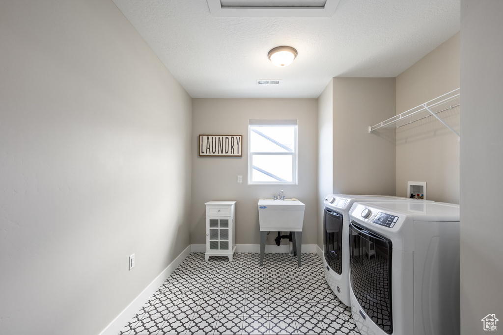 Clothes washing area with baseboards, visible vents, a sink, washer and clothes dryer, and laundry area
