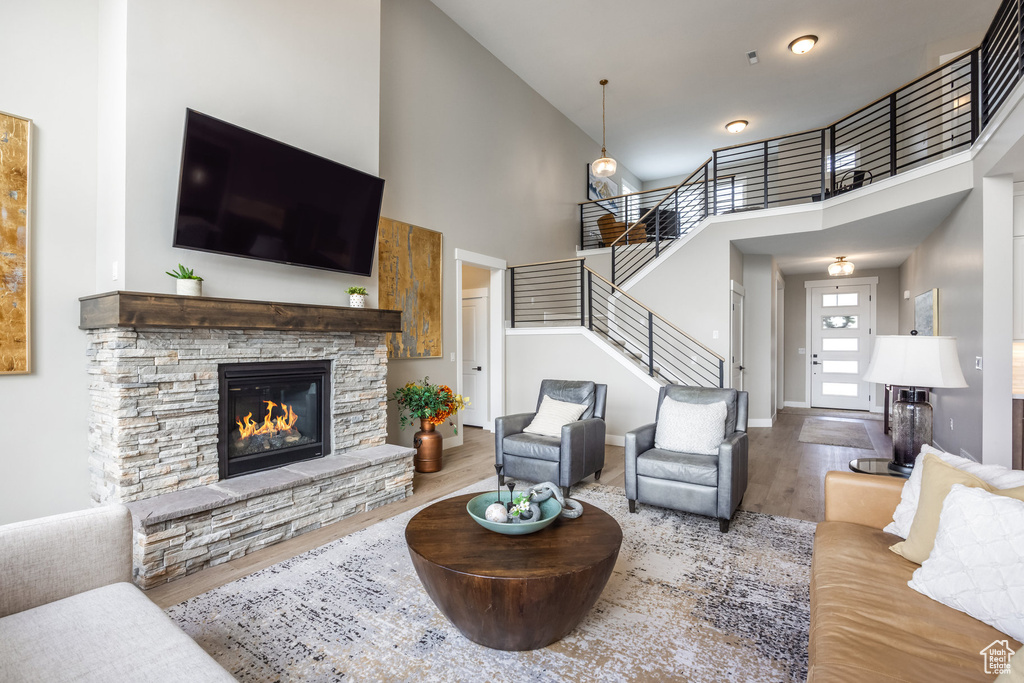 Living room with wood finished floors, high vaulted ceiling, a fireplace, baseboards, and stairs