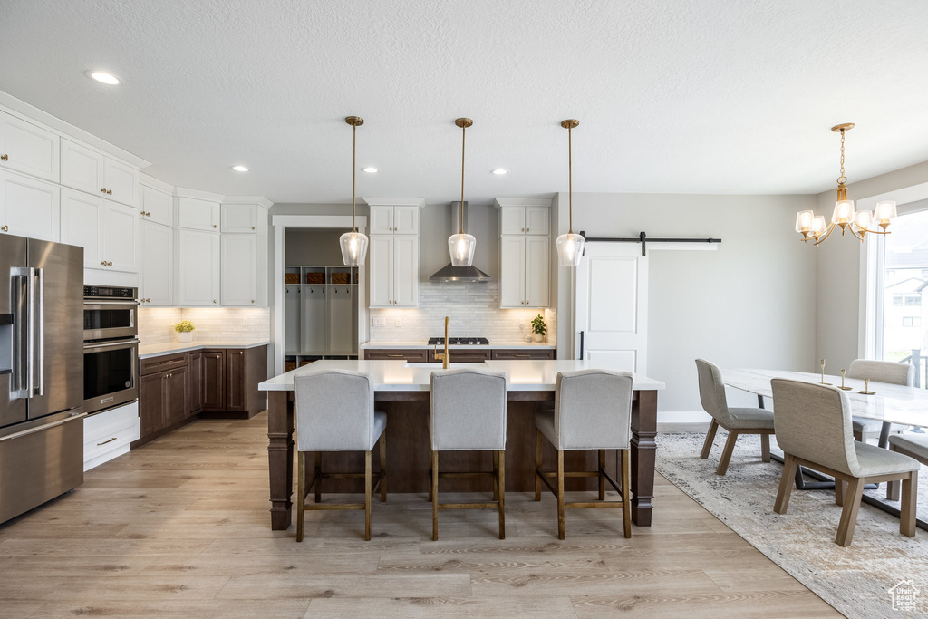 Kitchen with stainless steel appliances, wall chimney range hood, tasteful backsplash, a barn door, and light countertops