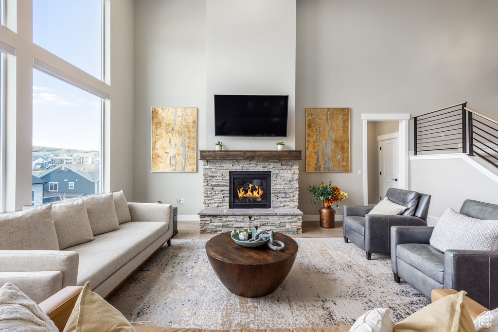 Living area with a stone fireplace, wood finished floors, baseboards, and a high ceiling