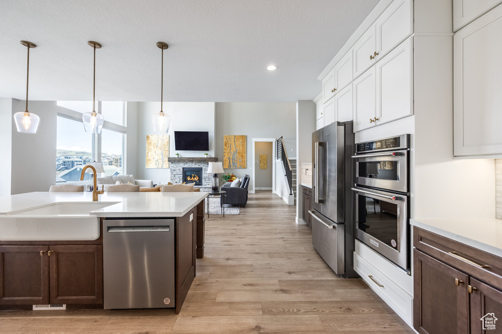Kitchen with a sink, stainless steel appliances, a fireplace, light wood-style flooring, and light countertops
