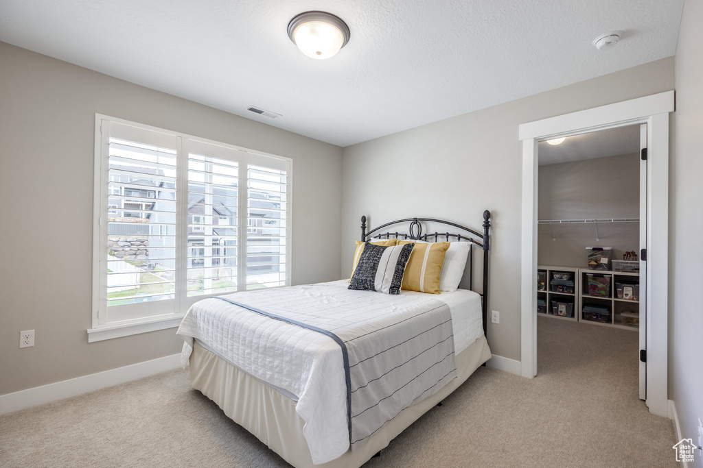 Bedroom with light carpet, visible vents, and multiple windows
