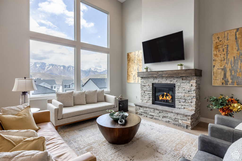 Living room featuring a stone fireplace, wood finished floors, baseboards, and a high ceiling