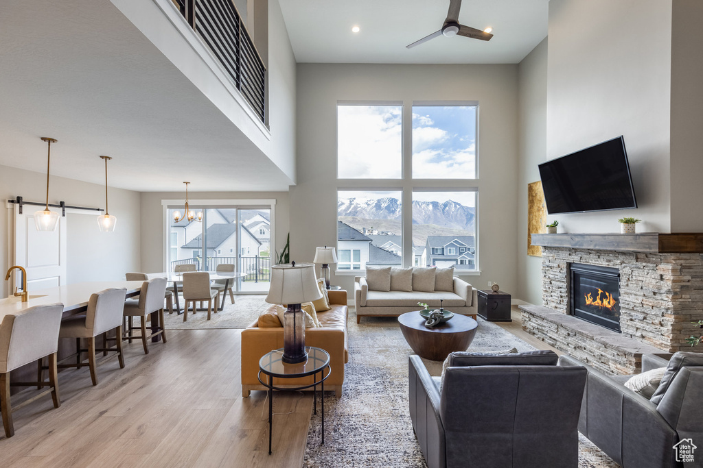 Living area featuring ceiling fan with notable chandelier, a fireplace, a towering ceiling, light wood-style floors, and recessed lighting