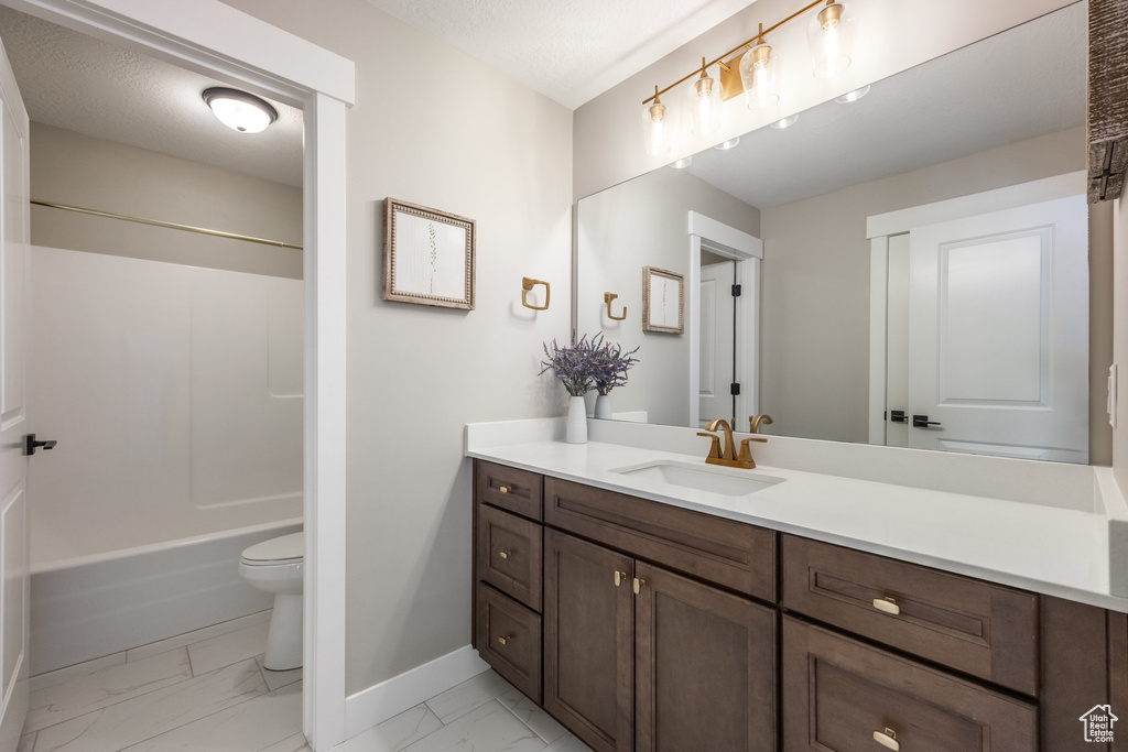 Bathroom with baseboards, marble finish floor, toilet, vanity, and shower / bathing tub combination