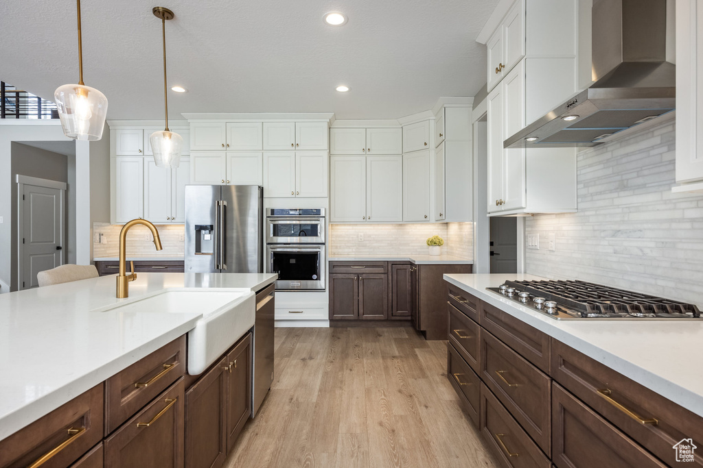 Kitchen with light countertops, wall chimney exhaust hood, stainless steel appliances, and white cabinetry