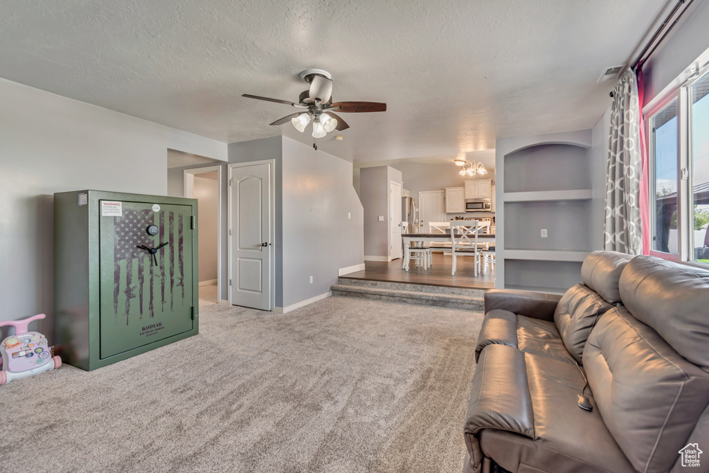 Living room featuring carpet floors, baseboards, ceiling fan with notable chandelier, and a textured ceiling