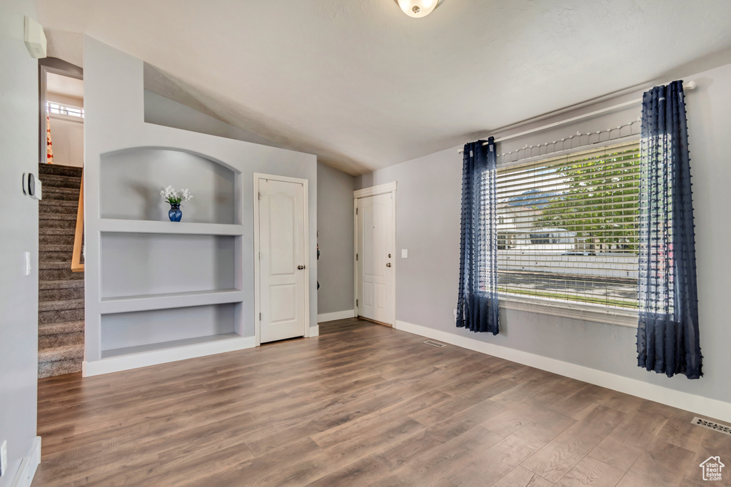 Unfurnished living room featuring built in features, stairs, baseboards, wood finished floors, and visible vents