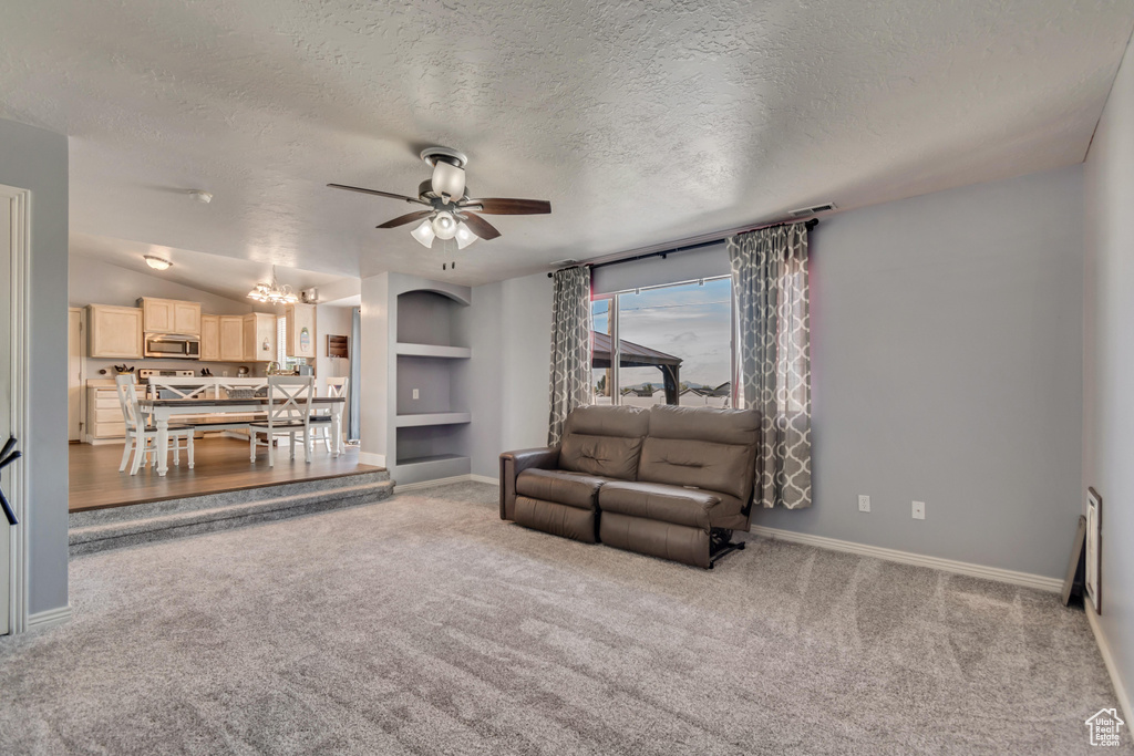 Carpeted living area with baseboards, ceiling fan with notable chandelier, and a textured ceiling