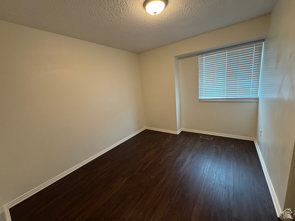 Spare room with baseboards, dark wood-style flooring, a textured ceiling, and visible vents