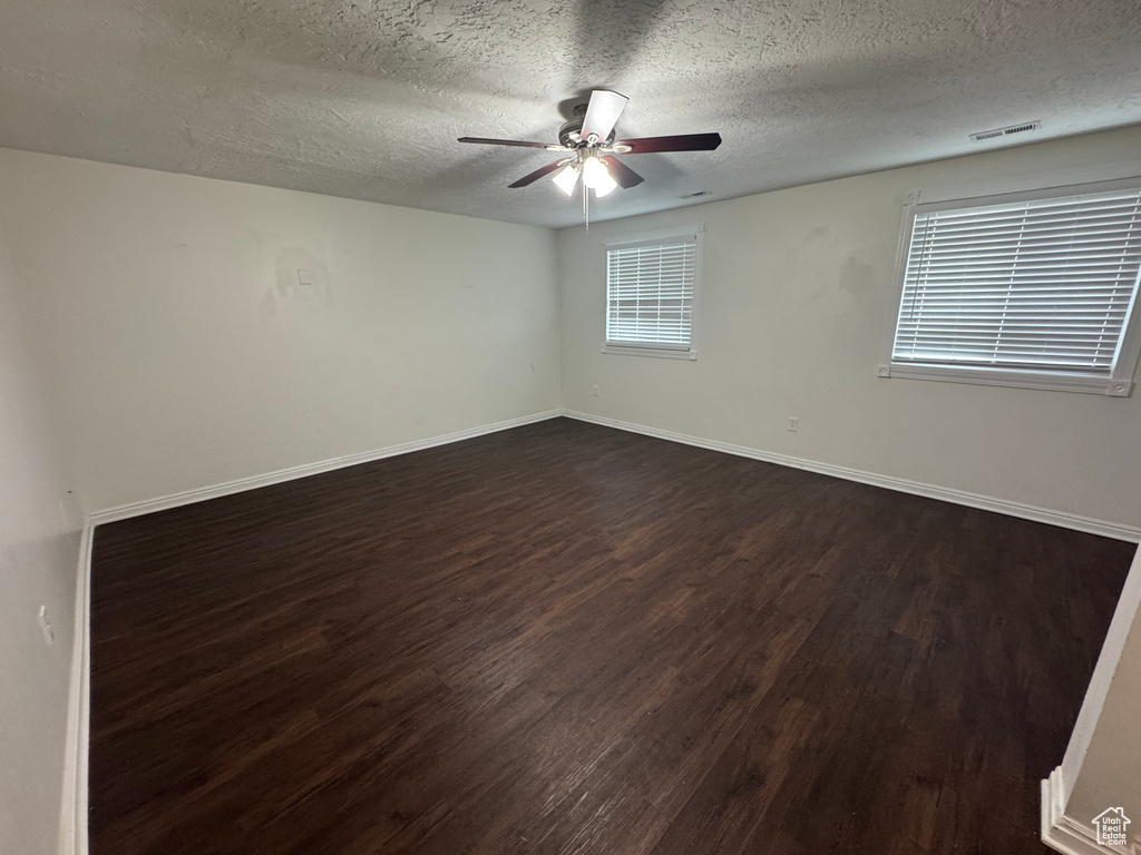 Unfurnished room featuring a textured ceiling, a ceiling fan, baseboards, dark wood-type flooring, and visible vents