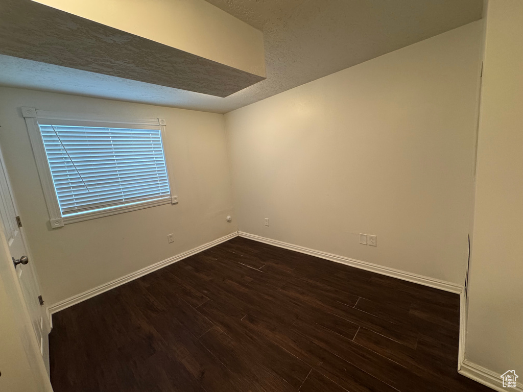 Empty room with baseboards, a textured ceiling, and dark wood-style flooring