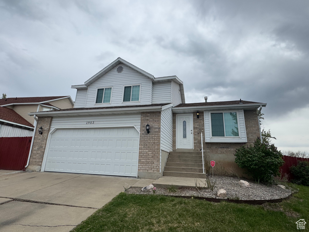 Tri-level home with brick siding, a garage, fence, and concrete driveway