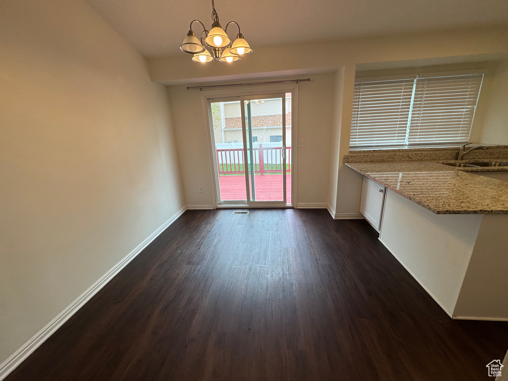 Unfurnished dining area featuring baseboards, a chandelier, dark wood-style floors, and a sink