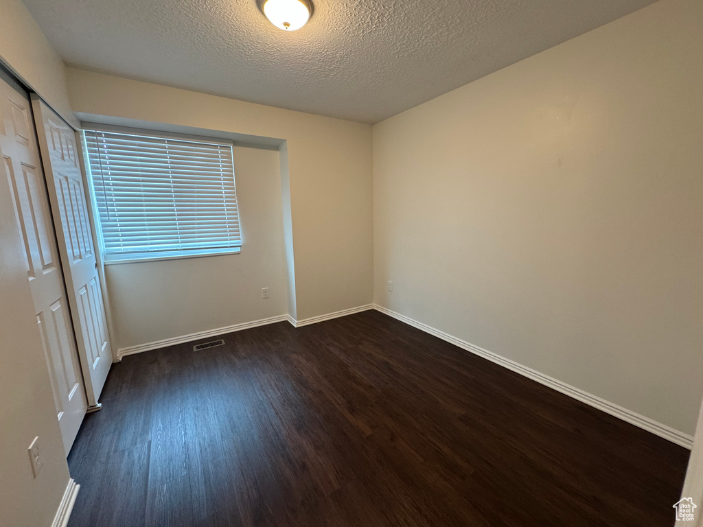 Unfurnished bedroom featuring a textured ceiling, visible vents, baseboards, a closet, and dark wood-type flooring